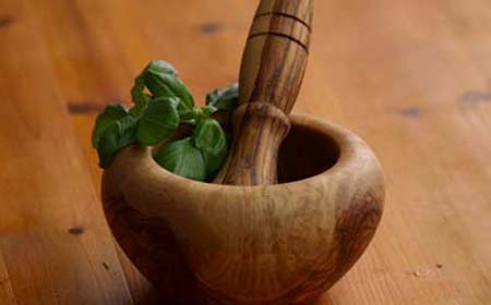 Préparation artisanale de médicaments à base de plantes, montrant une table en bois avec divers herbes fraîches et sèches, accompagnées d'outils traditionnels tels qu'un mortier et un pilon.